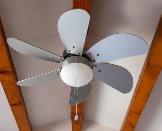 Ceiling fan with five alternating gray and white blades, a central light fixture, and pull chains, mounted on a ceiling with exposed wooden beams.