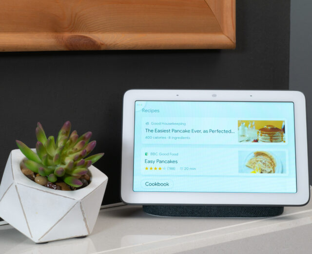 A smart display on a countertop shows pancake recipes next to a small potted succulent.
