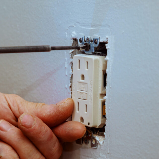 A technician tightening a screw while installing an electrical outlet.