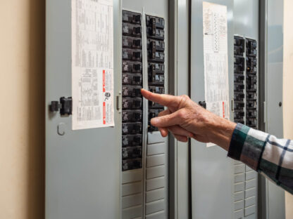 Male electrician turning off power for electrical outlet at circuit breaker box. Resetting tripped breaker in residential electricity power panel.