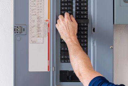 A person adjusts a breaker switch in an open electrical panel.