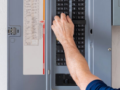 A person adjusts a breaker switch in an open electrical panel.