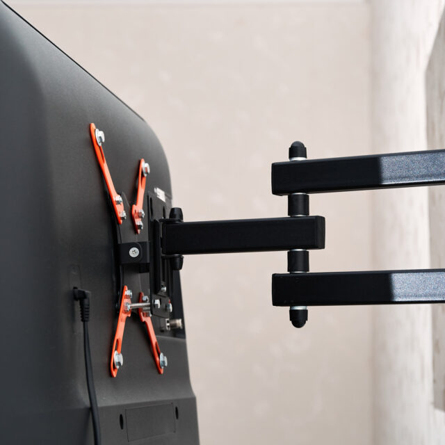 Back view of a wall-mounted flat-screen TV with an adjustable black and orange bracket.
