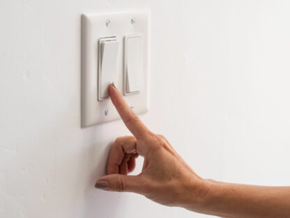 A hand reaching to flip a light switch on a white wall.
