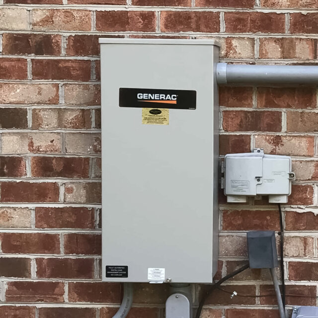 Outdoor Generac electrical panel mounted on a brick wall, with conduits and nearby utility boxes.