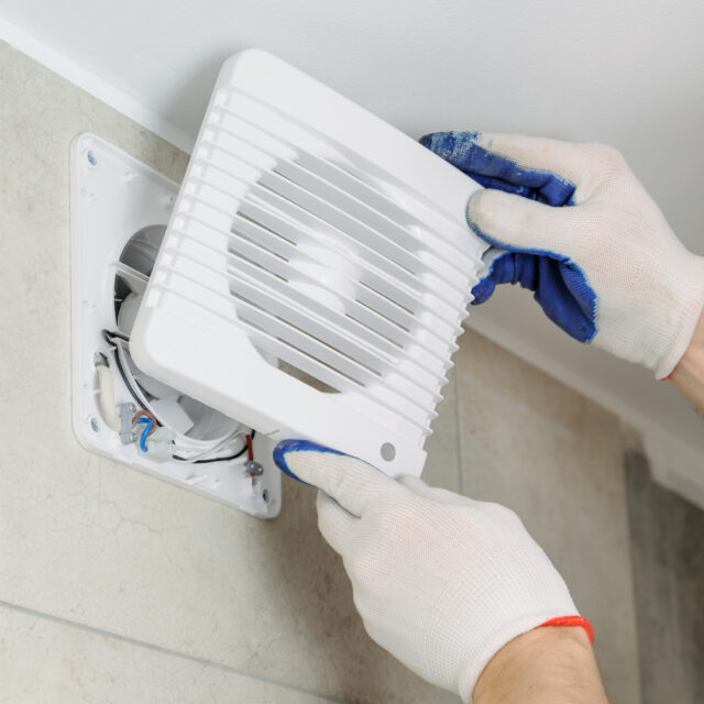 Person wearing gloves installs a white vent cover on a wall.