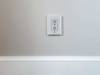 A white electrical outlet on a light gray wall above a wooden floor.