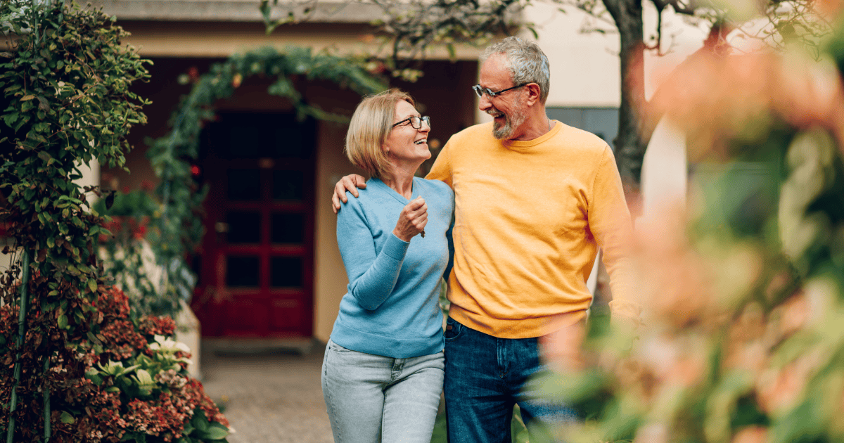 Retired couple smiling together in front of their house.