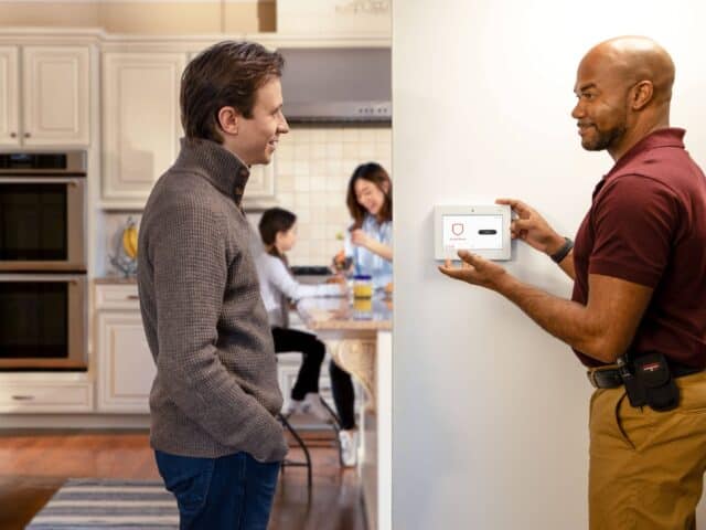 Dad speaking with a home security service technician in Texas who is explaining a newly installed home security system.
