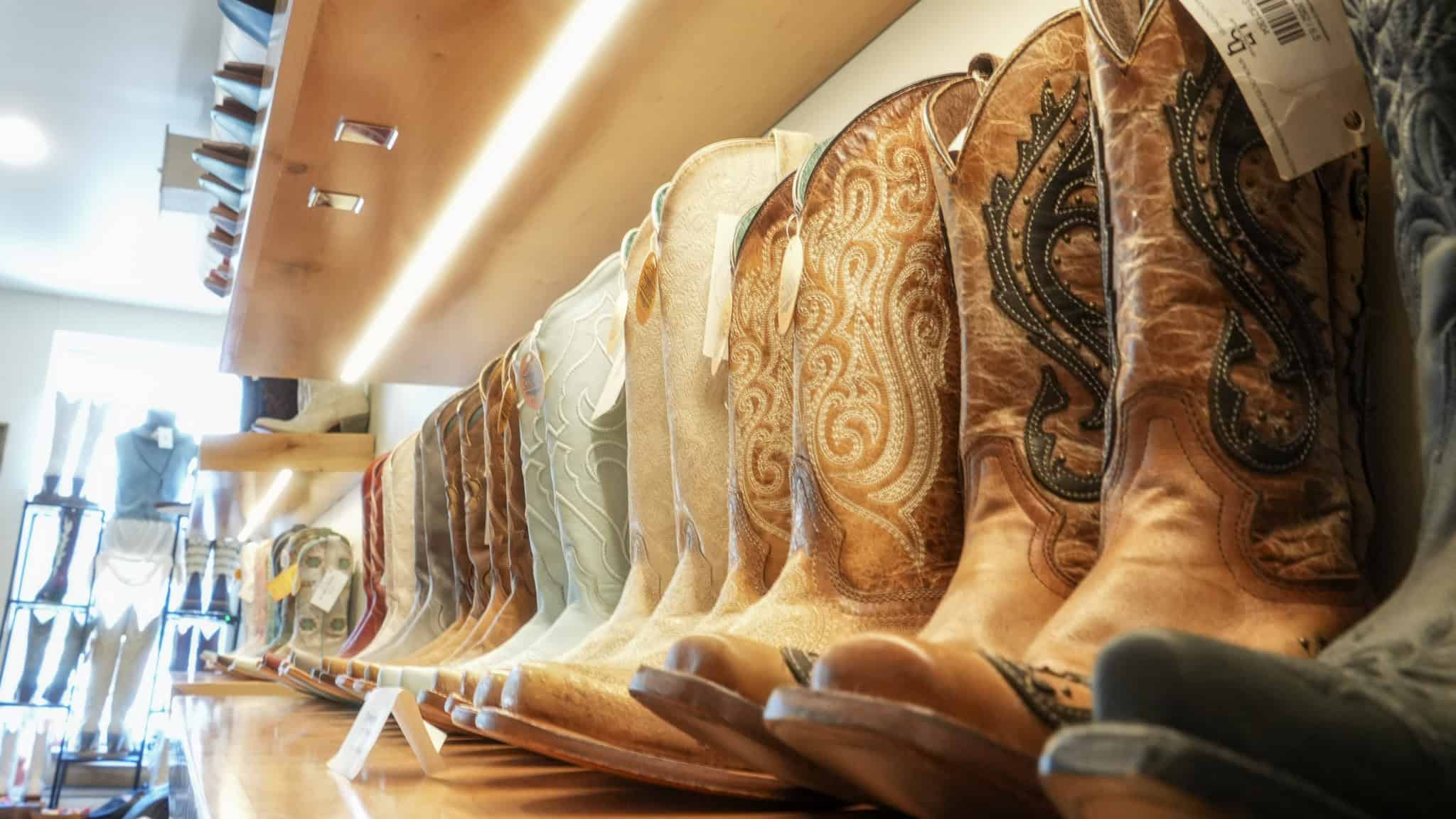 Boots lined up along a well-lit display shelf in downtown Texan boutique.