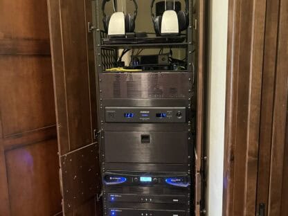 A tall, open wooden cabinet contains a rack with audio and electronic equipment, including two pairs of headphones on the top shelf.