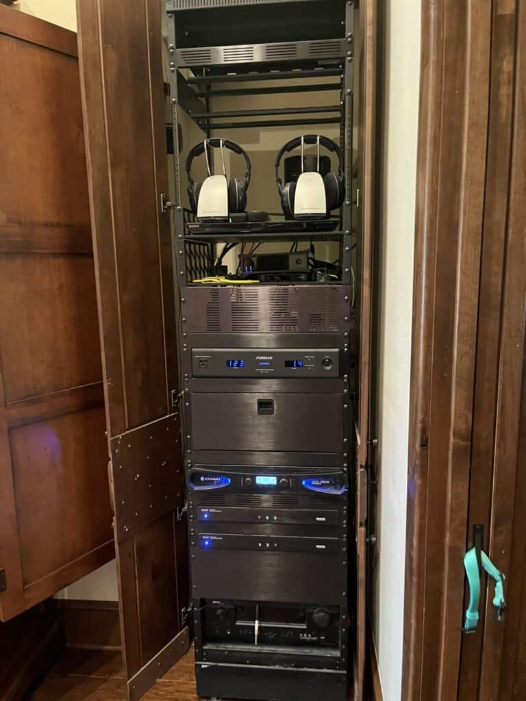 A tall, open wooden cabinet contains a rack with audio and electronic equipment, including two pairs of headphones on the top shelf.